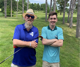 Four men smiling and standing shoulder-to-shoulder on a wide green fairway.