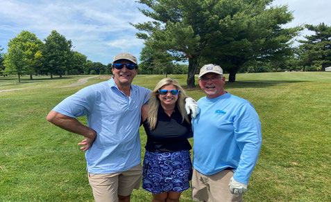 Four men in casual golf attire standing in a row on the green grass.