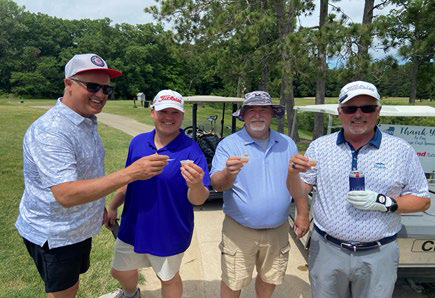 Four men holding up small shot cups to toast near a golf cart.