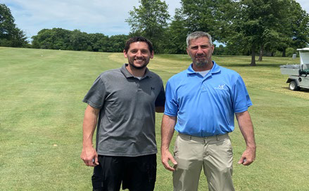 Two men standing side-by-side on an open, sunny golf fairway.
