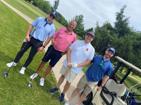 Four men in golf apparel standing together on a grass path.