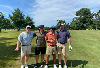 Four men smiling and posing together on a vibrant green fairway.