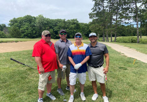 A group of four men posing together near a white golf cart on the course.