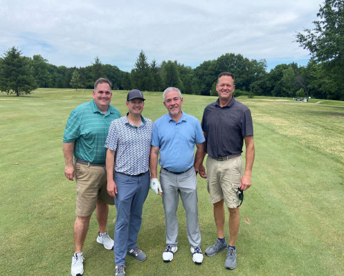 Four men in golf attire posing for a photo on a sunny day.